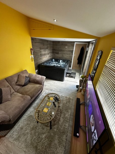 Cozy living space with a sofa, glass coffee table, TV, and a hot tub in the background.