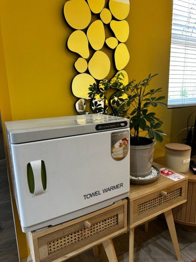 Small white fridge beside a potted plant and decorative round mirrors on a yellow wall.