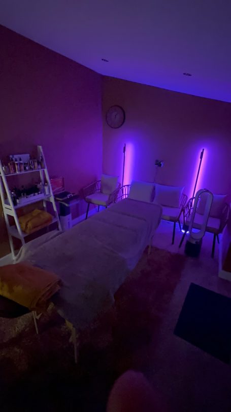 A dimly lit room with purple lighting, featuring a massage table and seating area.
