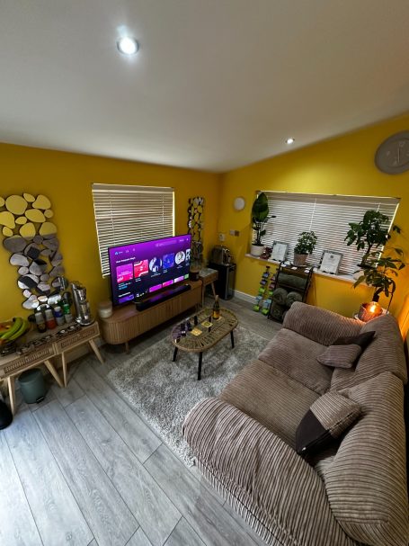 A bright living room with a large TV, yellow walls, plants, and comfortable seating.