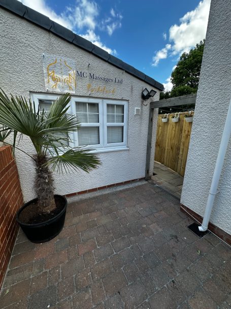 Exterior view of a building entrance with a palm plant in a pot and wooden gate.