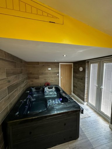 Interior view of a room with wooden walls and a hot tub under a yellow ceiling.