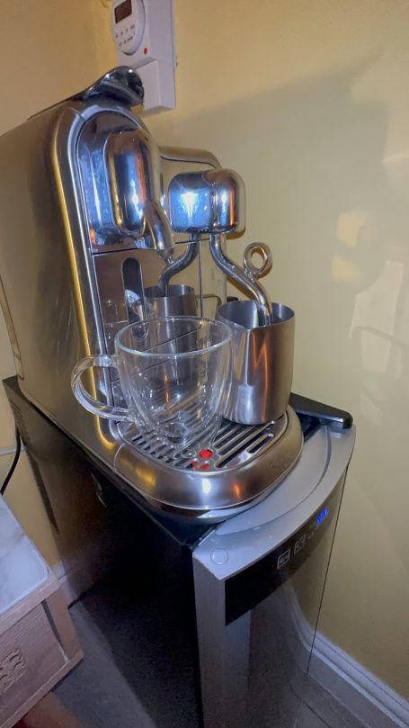 A sleek silver water dispenser with a glass pitcher beside it.