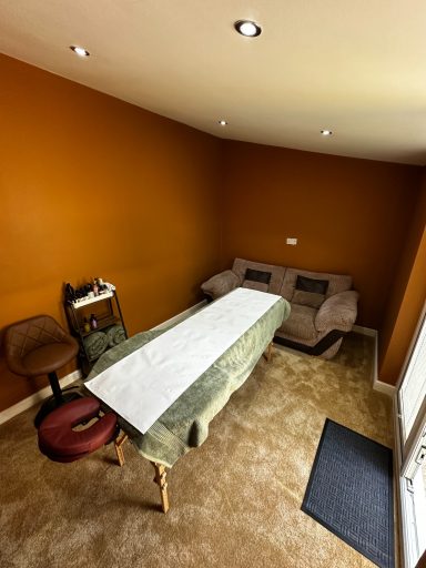 A small room with an orange wall, a table covered with a cloth, and a sofa.