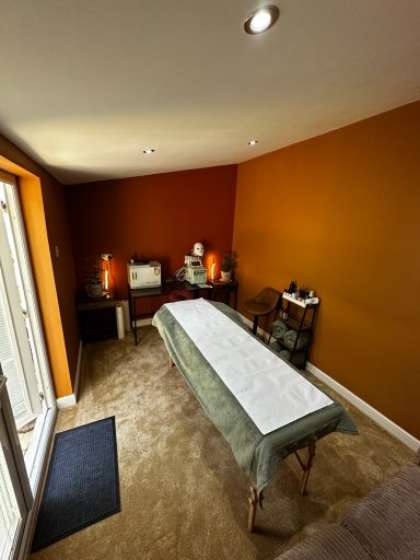 A treatment room with a massage table, warm orange walls, and soft lighting.