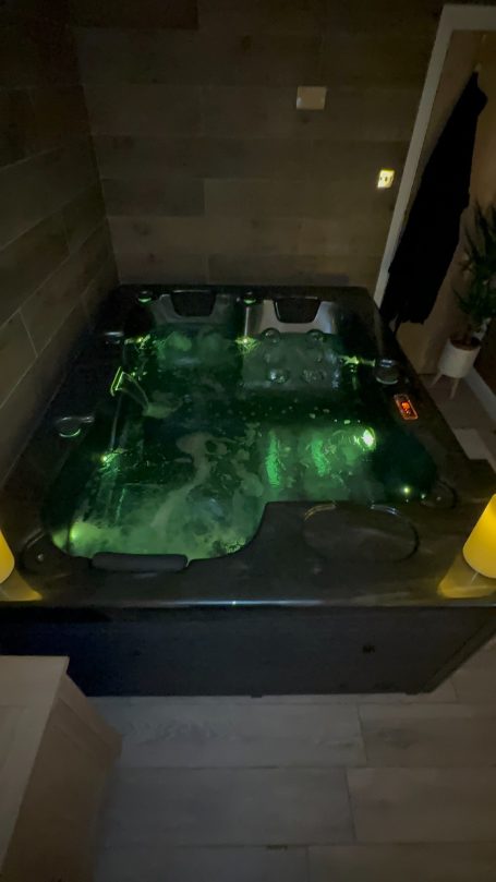 A luxurious hot tub with green lighting, surrounded by wooden walls.