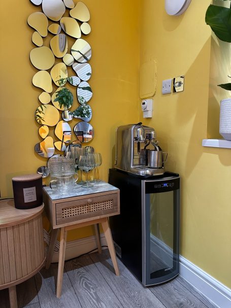 A modern corner setting with a mirrored wall, drinks cooler, and a decorative table.