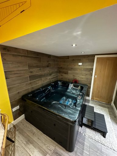 Hot tub situated in a wooden panelled room with yellow accents and a door nearby.